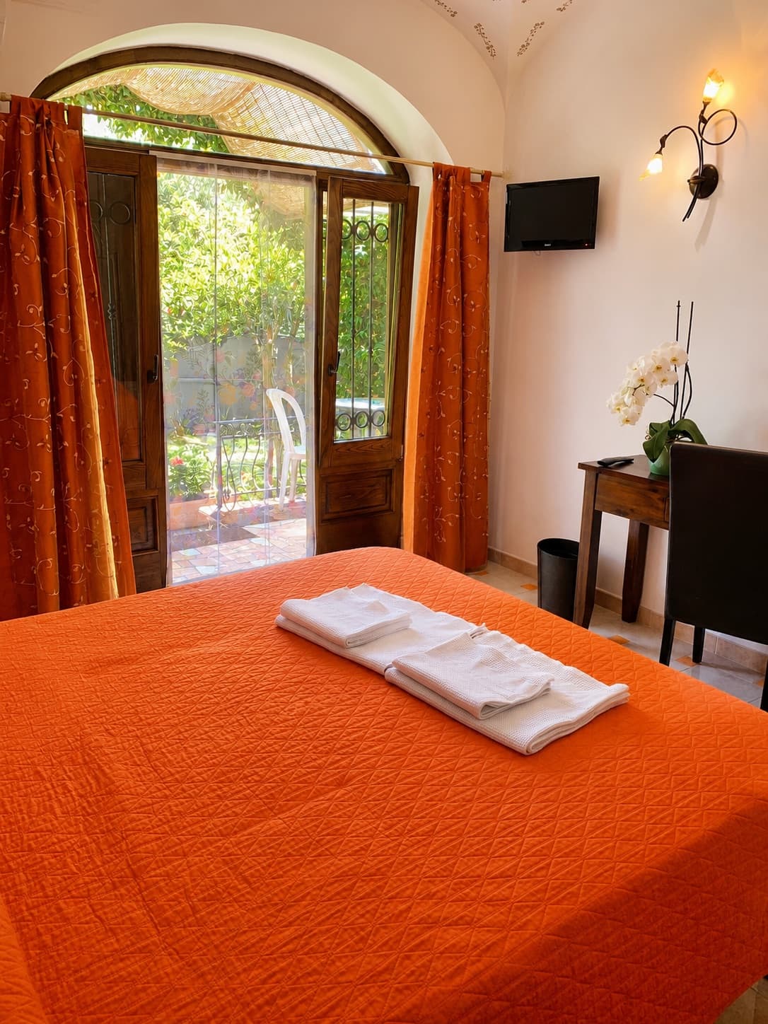 Double bed with an orange bedspread, facing an arched door open onto the garden